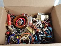 Large box filled with assorted jewelry including bracelets, bangles, necklaces, and pendants in various materials and colors.