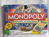 Box cover of Monopoly Here and Now featuring Mr. Monopoly and globe graphics, indicating world edition with electronic banking unit