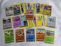 Mixed Pokemon card lot including some foil cards, featuring various Pokemon and Trainer cards spread out on a white surface.