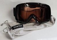 Front view of Smith ski and snowboard goggles with brown tinted lens resting on protective case.
