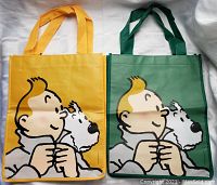 Two Tintin-themed reusable bags side by side on white surface. One bag is yellow-orange, the other green, both show Tintin and Snowy graphic.