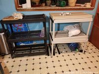 Two plastic shelving units in a kitchen setting, one black with three shelves and one white with two shelves, both around 3.5 feet high.