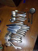 Overview of various spoons, forks, and knives laid out on a wooden surface showing some patina and wear.