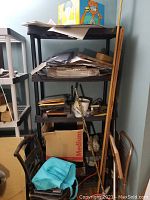 Black plastic shelving unit approximately 6 feet tall with four shelves, loaded with various items.