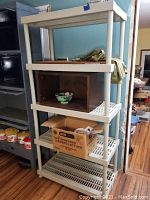 Full view of the shelving unit showing five shelves made of white plastic with grid patterned surfaces and open back and sides.