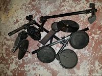 Overview of disassembled drum pads, cymbals, kick pedal, and metal rack on floor.