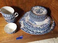 Full set of Johnson Bros blue and white porcelain plates, saucers, and tea cups arranged on wood shelf.