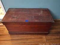 Full view of the antique wooden chest showing top and front panels with wear marks and medium-dark brown finish.