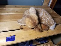 Baby deer stuffed animal laying on its side on wooden surface with a blue wall background.