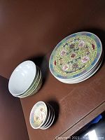 Full view of stack of large decorative porcelain plates and bowls with floral and symbolic patterns.
