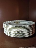 Stack of 8 white porcelain plates with scalloped edges and floral decorations viewed from the side.