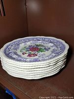Stack of 8 porcelain plates showing the floral and purple border design on the plate edges.