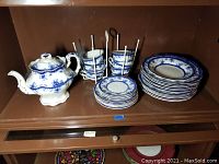 Full set on shelf showing teapot, cups in rack, saucers, and plates