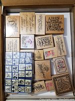 Large cardboard box of wooden mounted rubber stamps with a variety of inspirational quotes, friendship sayings, and decorative text, along with smaller stamp sets including colorful alphabet and Mickey Mouse character stamps.