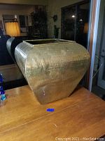 Side view of large bronze vase on wooden table, showing hammered texture and tapered square shape.