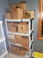 Three-tier shelving unit loaded with approximately 14 cardboard boxes labeled for clock movements