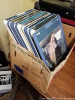 Laser disc collection stored upright in a worn cardboard box on a table, showing edges and spines of various discs including a Star Wars cover visible.