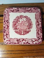 Top view of square porcelain cup holder showing red scenic motif and decorative grapevine border design