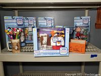 Full front view of all items on shelf showing Pez dispensers in mug, boxed Snoopy music box, multiple Charlie Brown Christmas figurines, mugs, and greeting card.