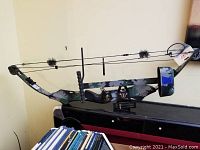 Full side view of PSE compound bow showing camouflage finish, string with dampers, wrist sling and adjustable sights.