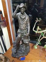 Full view of the cowboy statue on wooden surface next to a plant.