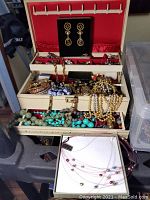 Full view of the fully packed cream-colored jewelry box showing multiple sections and compartments filled with assorted jewelry pieces including necklaces and bracelets