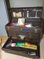 Viewed open metal tool box showing main compartment with various tools inside, including pliers and screwdriver sets.