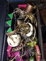 Photo of assorted women's costume jewelry including metal bangles, colorful bead bracelets, and rhinestone detailed pieces stored in a black wooden treasure chest.