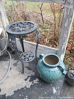 Full view showing the black wrought iron table and large blue pottery vase on a concrete floor.