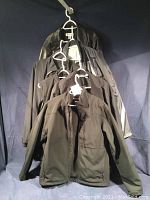 All six jackets/vests hanging on hangers against a dark backdrop showing varied colors including black and grey with some reflective elements