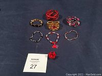 Overview of the lot showing seven bracelets laid out and one red flower ring in front.