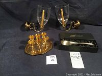 Full view of the lot showing the two brass wall-mounted candle holders with clear glass covers and candles inside, the shiny brass sherry glasses arranged on the brass serving tray, and the pewter-plated heron ladle in its box along with product sheet.