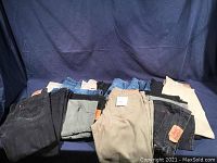 Photo showing various stacked men's jeans and pants in different colors and brands.
