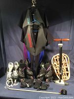 Full view of all items in lot including 2 wetsuits hanging, 2 pairs of roller blades, 2 sets of wrist guards, snow shoe, ice skates, bike pump and tape measure.