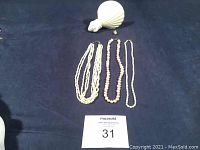 Full view of all jewelry items including the three pearl necklaces laid out on dark cloth background with the seashell nightlight at top and single pearl earring visible.