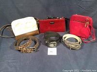 Full view of three crossbody bags and three belts laid out on a dark surface