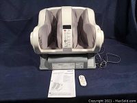 Full unit showing foot massager with padded foot beds, remote, and instruction manual in front on surface
