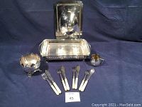 Full set of vintage silverplated fish dinnerware and serveware including forks, fish cutting tool, creamer, serving dish, and floral arrangement piece displayed on table with blue cloth background.