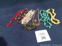 Lot of six stone and shell necklaces, one bracelet, and one pair of earrings laid out on a dark cloth background.