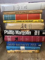 Spines of 11 hardback books in lot showing titles and authors including Phillip Margolin, David Baldacci, Anne McCaffrey.