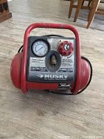 Front view showing pressure gauge, control knob, and Husky branding on compressor unit.