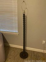 Full view of the black standing floor lamp; shows tall lamp standing upright with rounded segmented base and harp for shade attachment.
