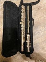 Clarinet disassembled into three pieces inside an open black fabric case with soft lining, showing the silver color and key mechanisms.