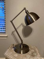 Photo of metal desk lamp on decorative table, showing full lamp with shade and articulated arm.