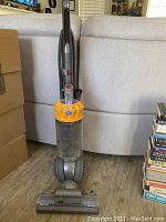Full view of the upright Dyson vacuum showing the yellow cyclone assembly, transparent dustbin with visible dust, grey ball base, and handle.