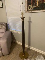 Full view of the standing floor lamp showing the tall wooden body with brass base and socket, no shade attached.