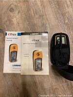 Photo of Garmin eTrex owner's manual, quick start guide and carrying case on wood floor.