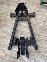 Black metal motorcycle/bike stand showing triangular base, adjustable locking mechanism, and securing arms.