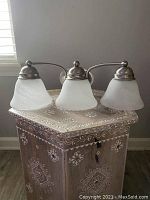 Three-light wall sconce with frosted white bell-shaped glass shades on a brushed nickel frame, resting on decorative table, side view