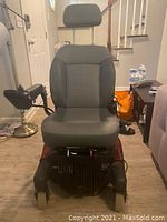 Front view of the Quickie Aspire electric wheelchair showing the seat, headrest, joystick controller on the right side, missing left arm rest, and base wheels.